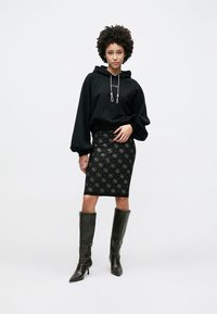 Μαύρο φαρδύ φούτερ με κουκούλα, εφαρμοστή μαύρη φούστα με γεωμετρικό μοτίβο και μαύρες μπότες μέχρι το γόνατο. Λείες υφές, άνετη εφαρμογή, μοντέρνο σχέδιο.