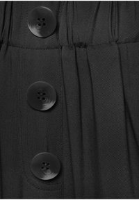 Schwarzer Stoff mit strukturiertem Gewebe, der vier große schwarze Knöpfe entlang der Vorderseite und plissierte Details unterhalb der Knöpfe aufweist.