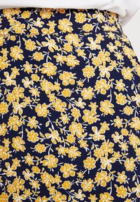 Jupe marine à motif floral avec de petites fleurs jaunes et des tiges vertes. Le matériau semble doux avec une texture lisse.
