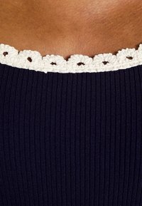 Gros plan sur un vêtement en tissu côtelé foncé avec un bord en crochet blanc le long de l'encolure sur une peau brune.