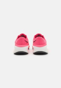 Par av träningsskor med en ljusrosa texturerad ovandel, vit mellansula och svart gummisula; subtil varumärkeslogotyp vid hälen.