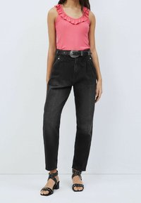 Czarne jeansy z wysokim stanem mają luźny krój, fałdy z przodu i szlufki na pasek. Połączone z różową bluzką bez rękawów z falbanami przy dekolcie.