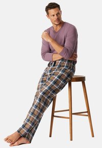 Paarse lange mouwen top gecombineerd met geruite pyjamabroeken in bruin, blauw en wit. De broek heeft een elastische tailleband en een losse pasvorm.