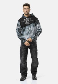 Zwart-grijze tie-dye hoodie met een voorzak en verstelbare trekkoord, gecombineerd met donkere cargobroek met meerdere zakken en verstevigde stiksels.