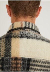 Koszula w kratę wykonana z flaneli z beżowymi, czarnymi i brązowymi wzorami. Miękka w dotyku, z kołnierzykiem i haftowanym detalem na plecach.