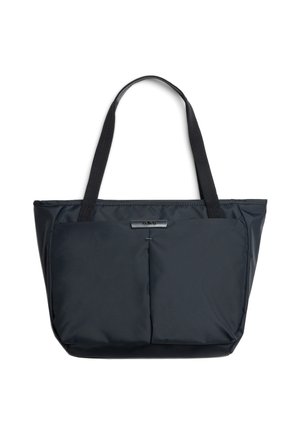 Borsa tote nera con due tasche frontali piatte, spallacci e una piccola targhetta rettangolare con logo sopra le tasche su sfondo bianco.