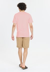 Vaaleanpunainen lyhythihainen t-paita yhdistettynä beigeihin polvipituisiin-shorteihin ja ruskeisiin liukuviin sandaaleihin, nähtynä takaa.