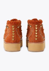 Pomarańczowe zamszowe botki za kostkę z puszystym kołnierzem, złotymi ćwiekami w kształcie serca oraz masywną beżową podeszwą, z ozdobnym przeszyciem i zdobieniami.