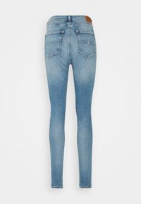 Jeans de denim ajustados, lavado azul claro, dos bolsillos traseros, textura desgastada y parche de cuero marrón en la cinturilla.