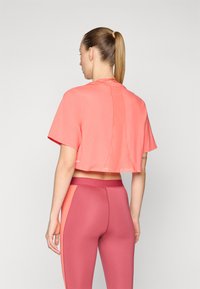 Korallfärgad kortärmad t-shirt i mjukt tyg, med detaljerad söm baktill. Matchas med rosa leggings med färgblockerade accenter på sidorna.