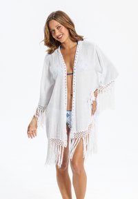 Copricostume kimono bianco con frange, realizzato in tessuto leggero, caratterizzato da un delicato pizzo lungo le maniche e l'orlo, design con apertura frontale.