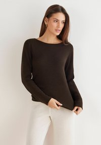 Brauner Pullover mit langen Ärmeln aus weichem Material, mit breitem Ausschnitt, eng anliegenden Bündchen und glatter Textur, kombiniert mit hellen Hosen.