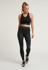 Svart idretts-BH med logo, kombinert med svarte leggings med teksturerte mønstre og sidestriper, komplettert med svarte og grå joggesko.