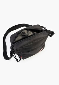 Black fabric crossbody bag with a zippered closure, featuring an adjustable strap and a small logo patch on the front. Smooth interior lining.