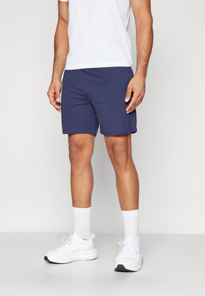 Bermudas de algodón azul marino con un corte relajado, que cuentan con una cinturilla elástica. Combinadas con una camiseta blanca y zapatillas deportivas blancas.