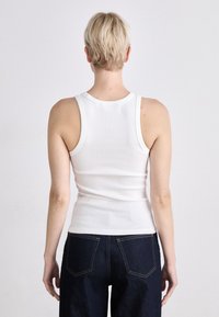 Weißes, geripptes Tanktop mit einem klassischen Rundhalsausschnitt und Slim-Fit, kombiniert mit dunkelblauen, hoch taillierten Jeans. Einfaches, unaufdringliches Design.