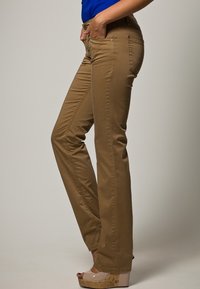 Bruna, raka byxor i mjukt tyg; har sidfickor och diskret sömnad; bärs med en blå topp och ljusbruna plattformsskor.