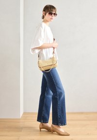 Hvit, løstsittende topp; høyt liv, utsvingte blå jeans; beige vevd håndveske med kjedehank; beige vevde hæler; solbriller.
