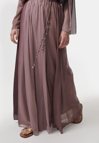 Lange, vloeiende rok in een verloop van zachte mauvetinten, gemaakt van doorschijnende stof met een elastische tailleband en decoratieve strikken. Sandalen zichtbaar.