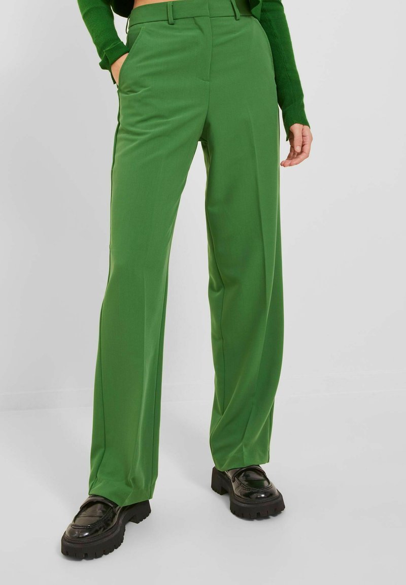 Groene high-waisted broek van soepel materiaal met een recht ontwerp, voorzien van zijzakken en een getailleerde pasvorm. Zwarte chunky schoenen.