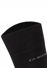 Calcetín negro hasta el tobillo con un diseño de punto texturizado, que presenta una banda suave en la parte superior y un detalle de etiqueta impresa en el lado en gris.