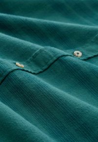 Teal stof met een zachte textuur, met horizontale strepen. Zichtbare off-white knopen voegen detail toe aan het ontwerp.