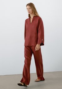 Haut en lin rouge avec un col en V et des manches longues, assorti à un pantalon large de même tissu. Présente des lignes épurées et une texture lisse.