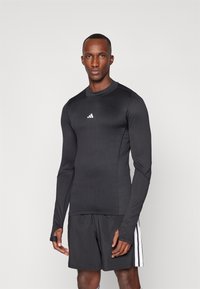 Schwarzes Langarm-Sportshirt aus Stretchmaterial mit Rundhalsausschnitt und weißem Adidas-Logo, kombiniert mit schwarzen Shorts.