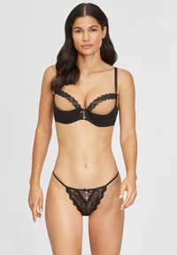 Zwart kanten lingerie set met een balconette-beha met golvende randen en een strikdetail in het midden, aangevuld met bijpassende doorschijnende slipjes.