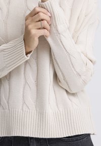 Svijetlobežasti pleteni džemper s uzorkom pletenica i rebrastim manžetnama. Ima teksturirani završetak i blago opušten kroj.