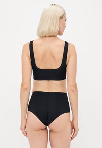 Svart badetøysett med en kvadratisk utringning bralette og høy midje bukse, begge med en glatt tekstur og minimale sømmer.