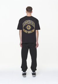 Černé pánské tričko s oversized střihem, na zadní straně s žlutým grafickým potiskem, který obsahuje nápisy "PEGADOR" a "BUILT TO LAST." V kombinaci s černými zúženými tepláky.