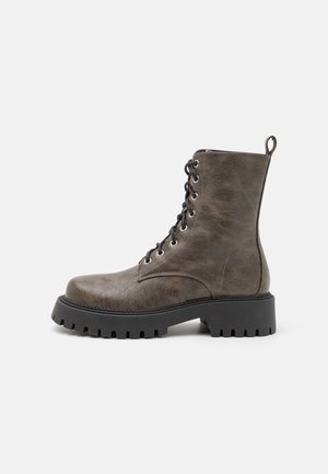 Brown faux leather ankle boot with black laces, round toe, thick black sole, and pull tab on the back. Textured surface with subtle shine.