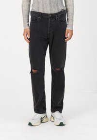 Svarta denimjeans med avslappnad passform, märkbara knärep, fem fickor och knappstängning. Bärs med vita sneakers.