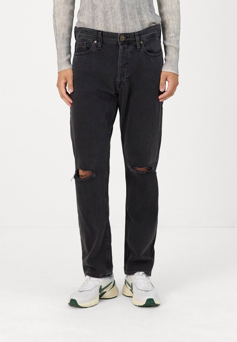 Svarta denimjeans med avslappnad passform, märkbara knärep, fem fickor och knappstängning. Bärs med vita sneakers.