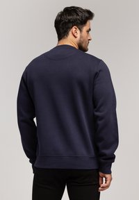Granatowy sweter z długimi rękawami, okrągłym dekoltem oraz prążkowanym wykończeniem. Wykonany z teksturowanej tkaniny, zaprojektowany z myślą o luźnym kroju.
