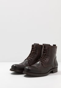 Botas de cuero marrón con cordones, punta redondeada y costuras decorativas. Altura hasta la mitad de la pantorrilla con una suela resistente y un tacón modesto.