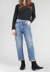 Top negro de manga larga con textura acanalada y escote redondo, combinado con jeans rectos azul claro desgastados y botines negros.