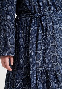 Mörkblå långärmad klänning med svart och vit ormskinnsmönster, med ett knytbälte i midjan och en volangkjol.