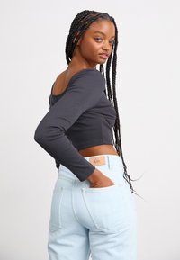 Gray long-sleeve cropped top paired with light blue high-waisted jeans. The jeans feature a tan label on the back pocket.
