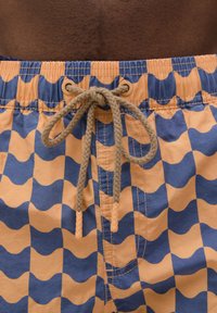 Shorts de bain avec un motif en vagues orange et bleues. Dotés d'une taille à cordon de serrage et de détails cousus. Fabriqués en tissu léger.