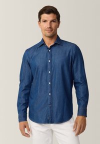 Camicia di jeans blu scuro con maniche lunghe, chiusura a bottoni sul davanti, colletto appuntito e bottoni bianchi. Texture morbida con orlo curvo.