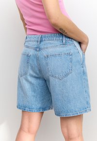 Lyseblå denimshorts med løs pasform, fem lommer og synlige syningsdetaljer. Stoffet fremstår blødt med en let tekstur.
