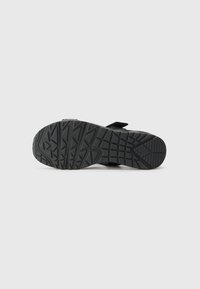 Black rubber shoe sole with a textured grip pattern, featuring deep grooves and a reinforced heel. The design is functional and durable.