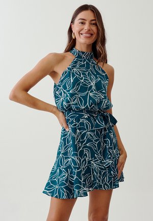 Tirkizna halter haljina s bijelim uzorkom lišća, dobro prilagođena korzetu, suknja koja se širi i ima slojevite falde, i detalj remena u istoj boji. Mekani, lagani materijal.
