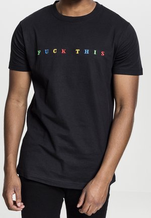 Person iført en sort kortærmet T-shirt med flerfarvede bogstaver, der staver en grov frase over brystet.