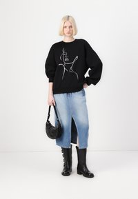 Hanorac negru cu un design din artă liniară albă, fustă din denim albastru cu o deschidere, cizme negre până la genunchi și o geantă rotundă neagră, cu studs.