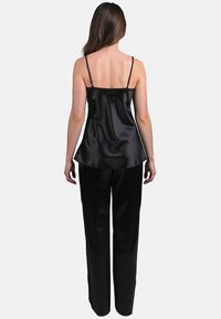 Camisole negru din satin cu bretele subțiri și siluetă fluidă, asociată cu pantaloni largi asortați, având o textură netedă și lucioasă.