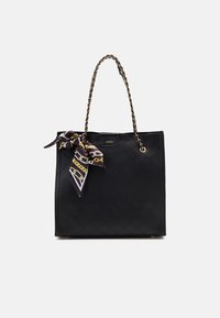 Bolso de tote acolchado negro con un asa de cadena trenzada y una bufanda de seda decorativa en púrpura y dorado atada al asa.