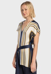 Blusa leggera color crema con righe verticali blu navy e oro, con scollo a V e maniche corte, arricciata in vita con un laccio abbinato.